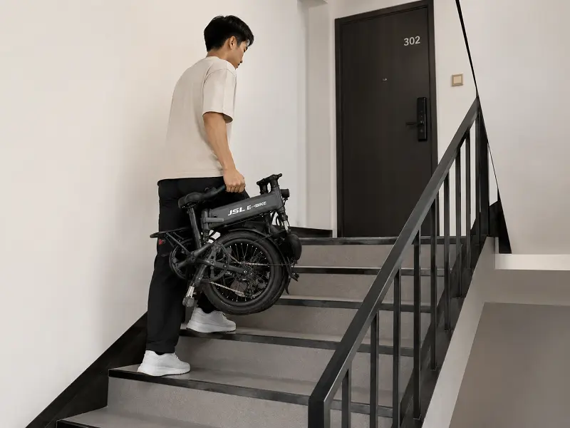 Portable 20-inch folding e-bike for city living A person easily carrying a folded 20-inch e-bike up the stairs of an apartment building.