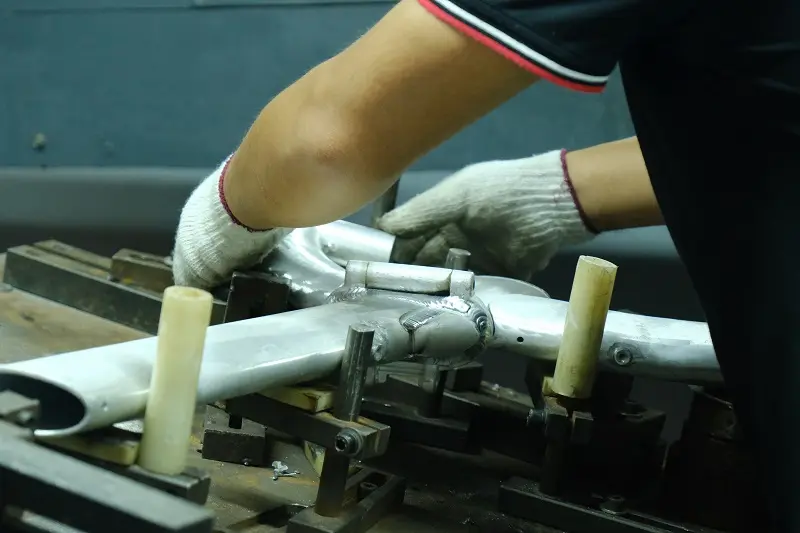 A factory worker using a precision tool to measure the alignment of a bicycle frame on a jig.